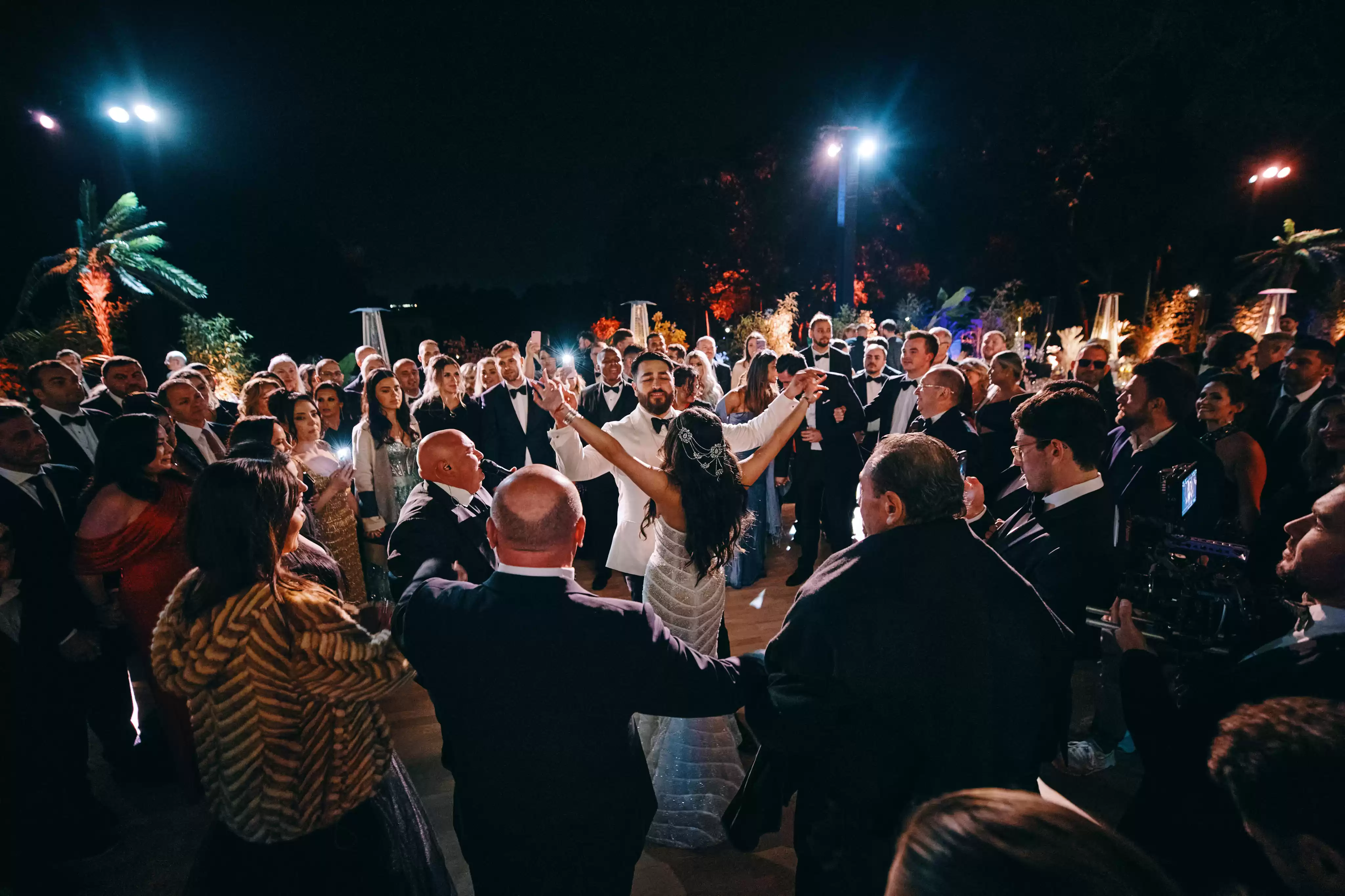 Soirée de mariage festive et inoubliable en extérieur, avec les mariés dansant de joie au centre de leurs invités sous les projecte