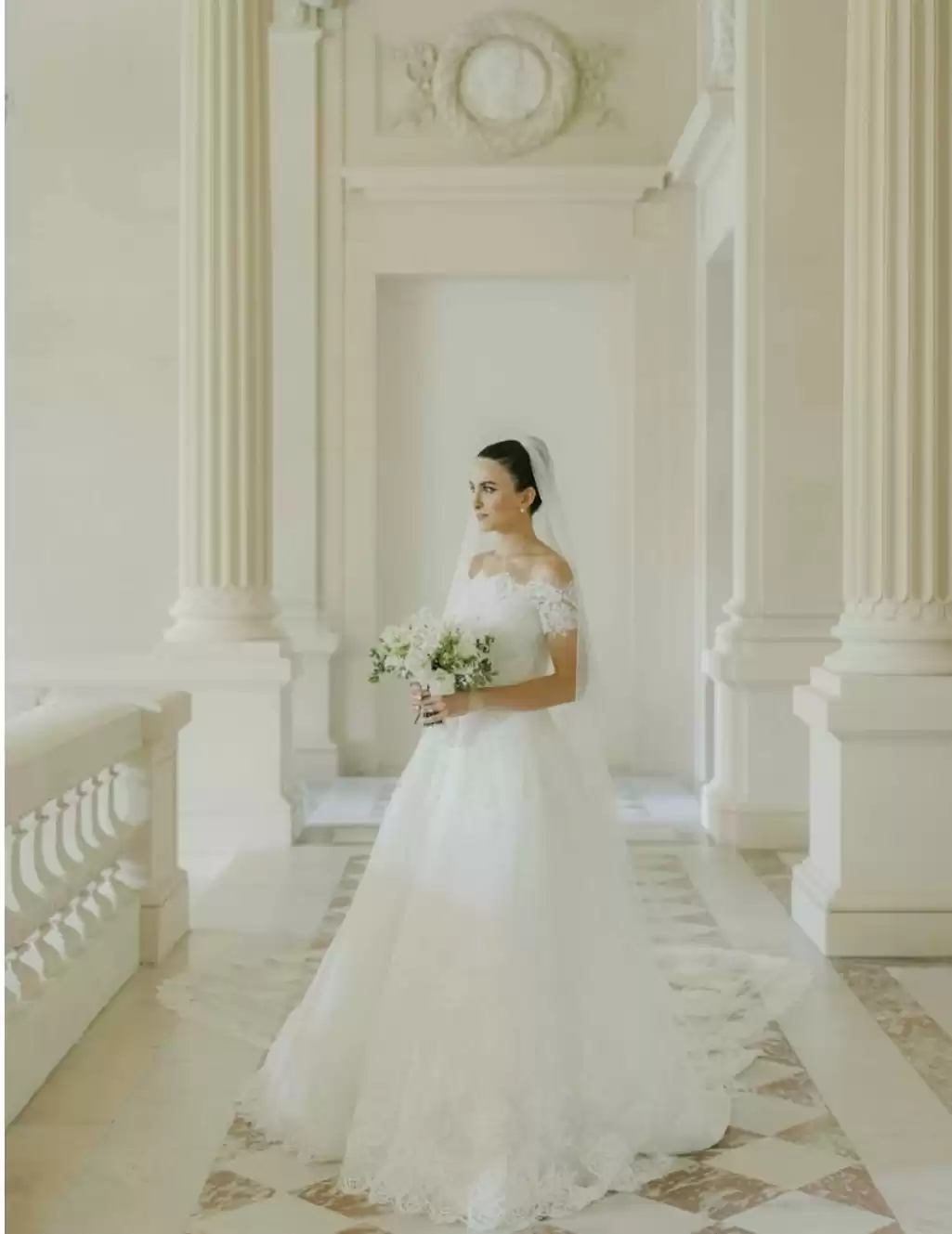 La mariée, vêtue d'une robe élégante et d'un long voile, se tient sur le Palier d'Honneur, un décor majestueux sublimé par des colonnes imposantes et une architecture clas