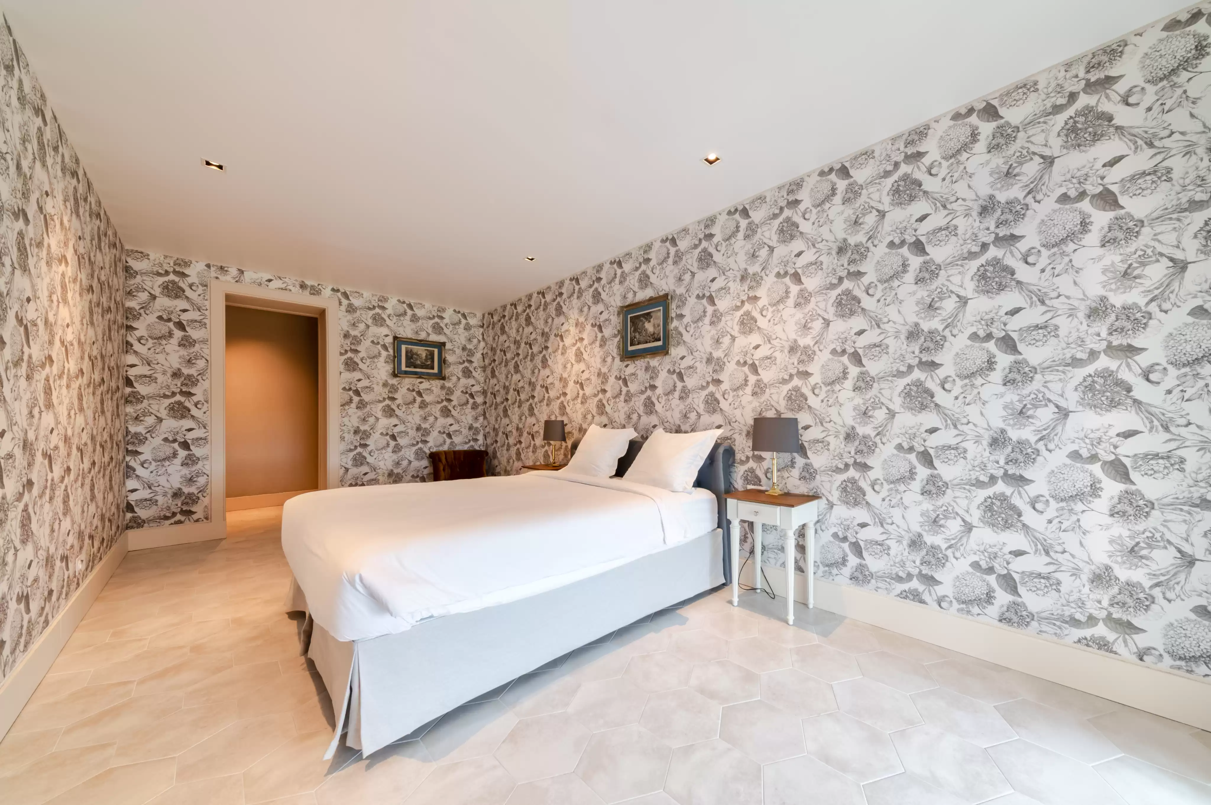 Chambre contemporaine au deuxième étage avec un papier peint floral noir et blanc distinctif, un grand lit confortable et un sol en carreaux clair