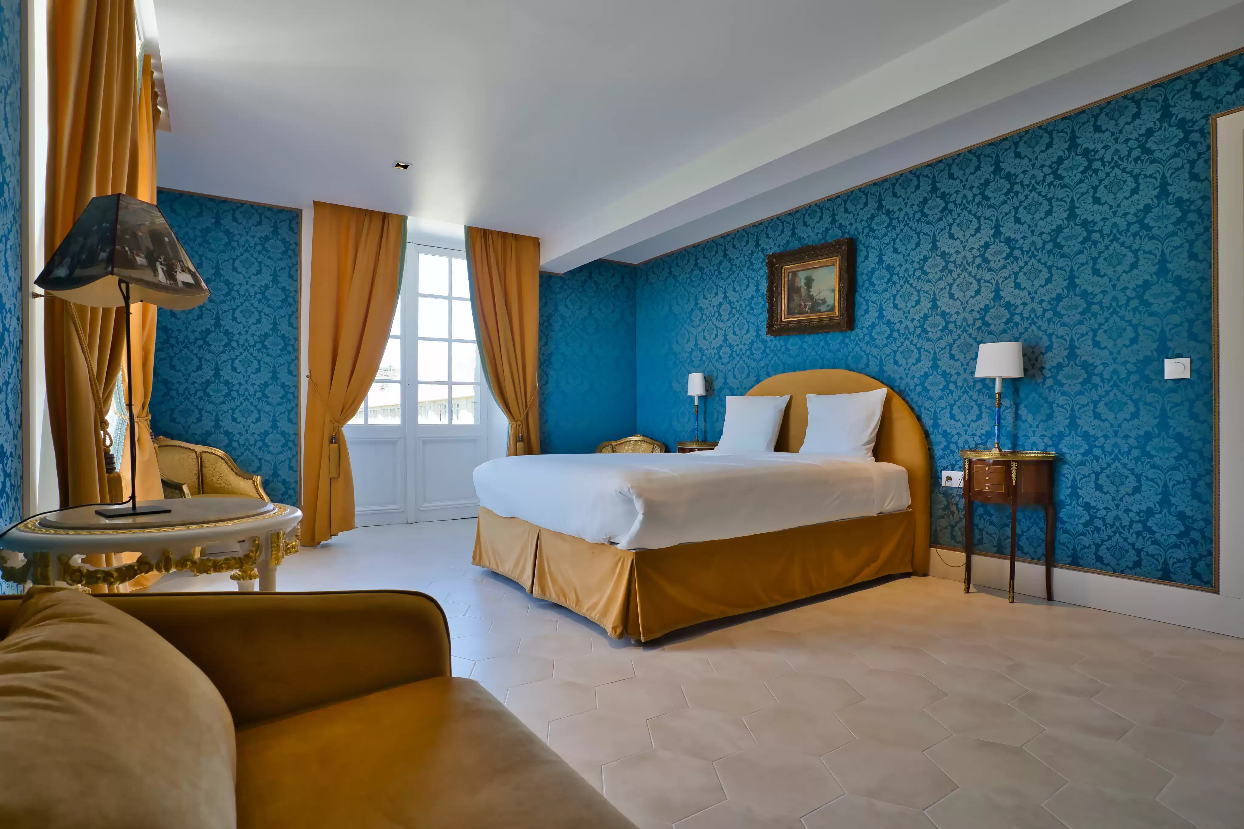 Spacieuse suite familiale au cadre chaleureux et raffiné, dotée de murs en papier peint bleu damassé, de rideaux dorés, d'un grand lit confortable et d'un can