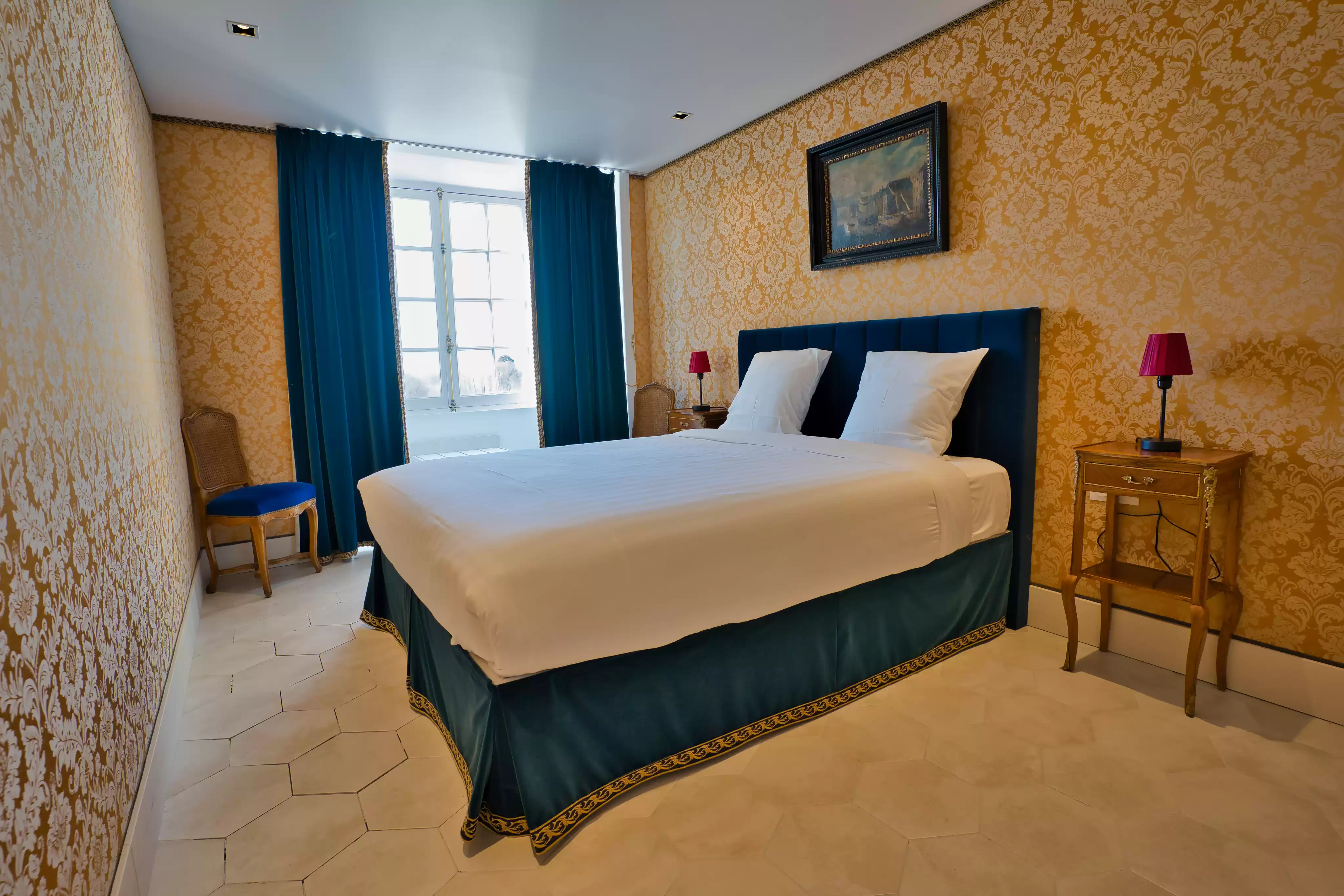 Seconde chambre de la suite familiale décorée d'un élégant papier peint damassé doré, contrastant avec un lit double et des rideaux en velours bleu pr