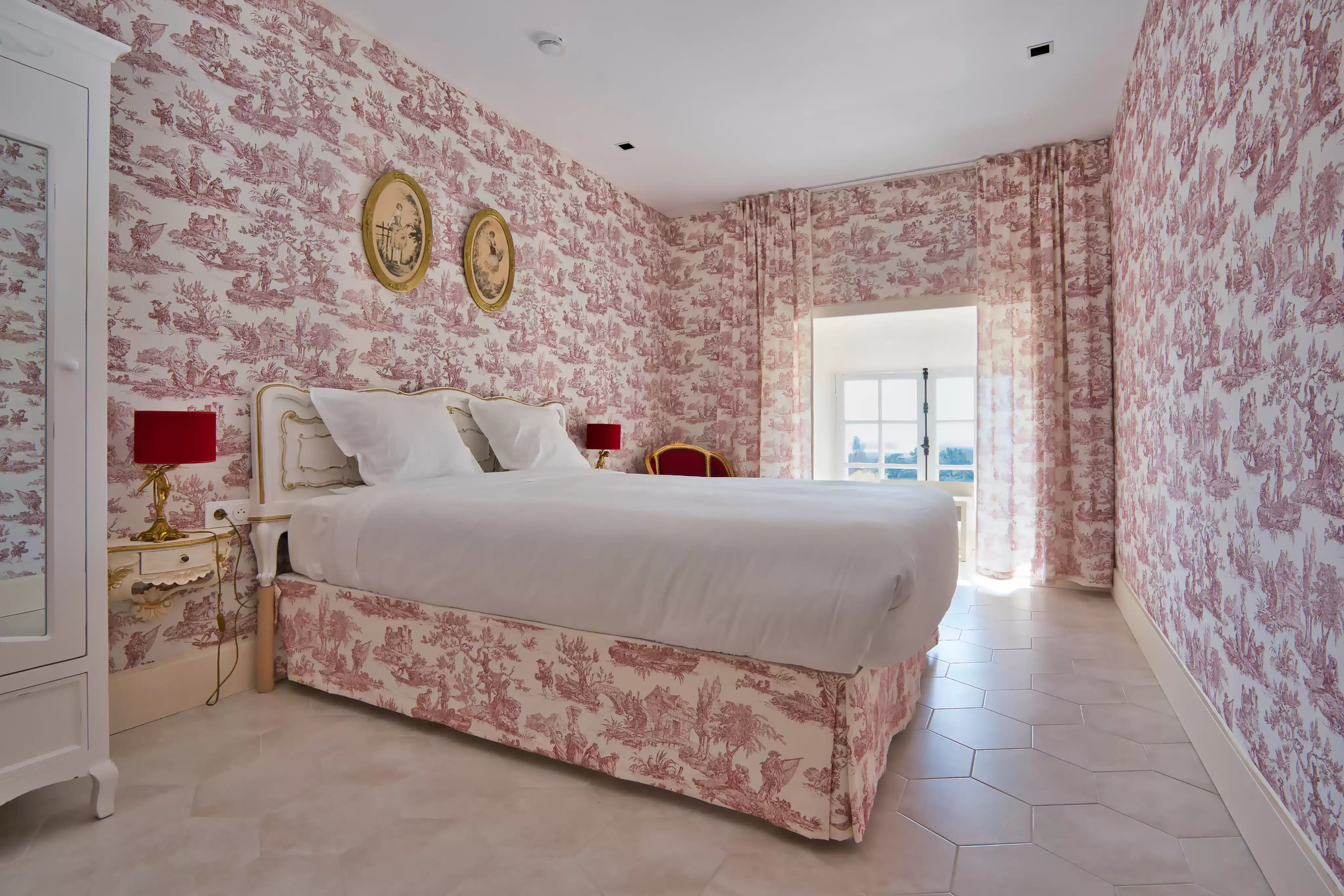 Chambre de charme lumineuse, entièrement décorée d'un papier peint et d'un cache-sommier assortis en Toile de Jouy rouge et blanc, avec un grand lit à tête de lit bla