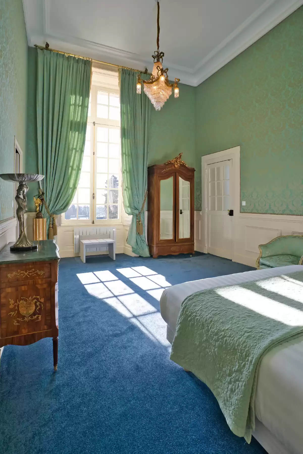 La Chambre des Mariés, élégante et pleine de caractère, baignée de lumière, avec des murs et rideaux verts profonds, une moquette bleue, un mobilier ancien et un lit d'amoureux vénitien s