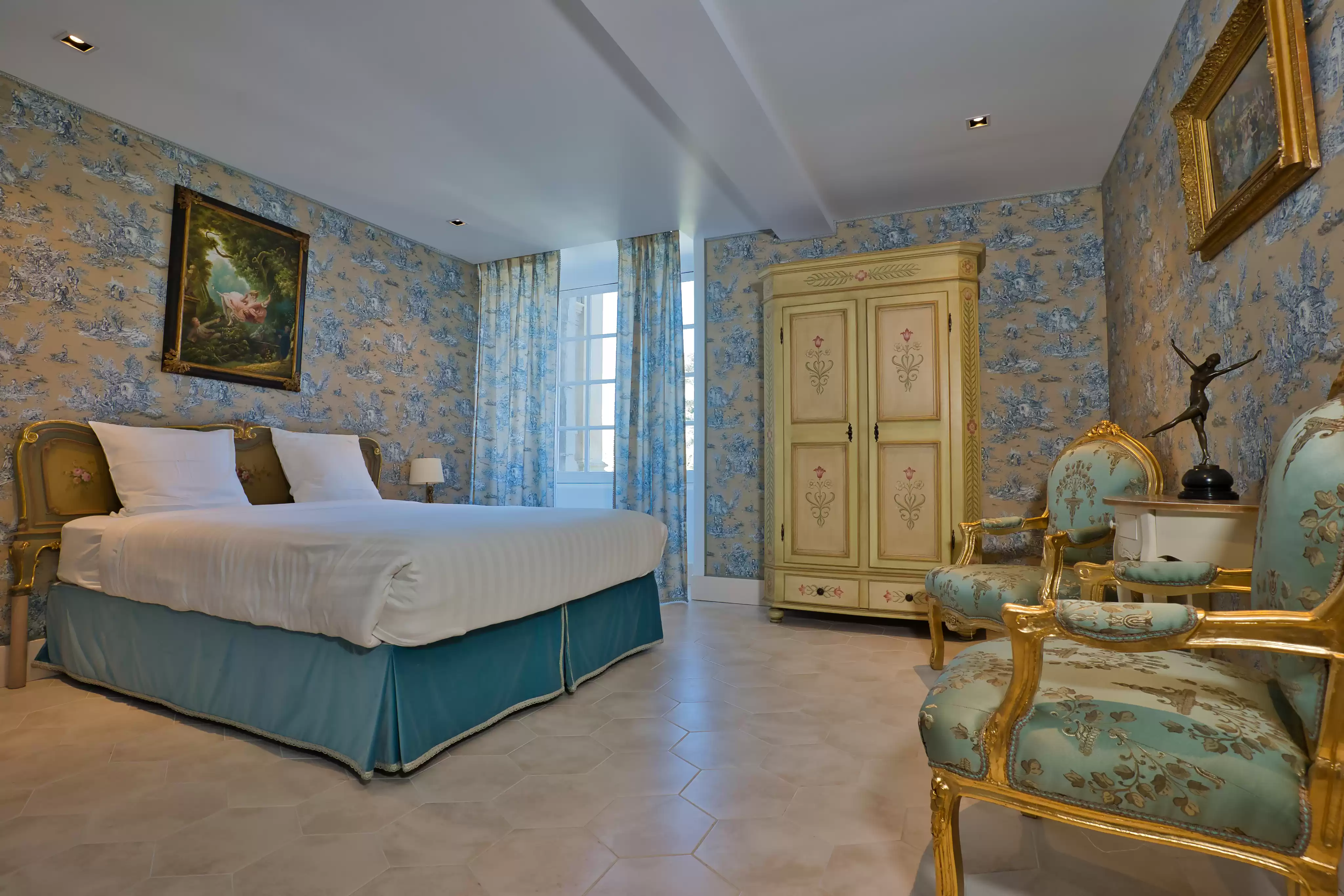 Chambre de château à l'élégance simple, dotée d'un papier peint à motifs bleus et dorés, d'un mobilier d'époque raffiné comprenant deux fauteuils et une armoir